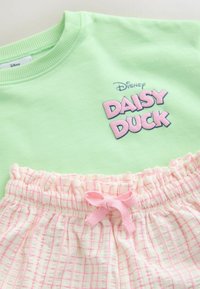 Világoszöld pulóver "Daisy Duck" rózsaszín felirattal. Fehér rövidnadrág rózsaszín rácsmintával és rózsaszín masnival a derékrészen.