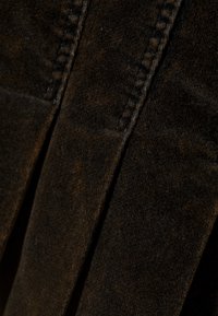 Tamno smeđi plisirani materijal s mekim teksturom i vidljivim šavovima, koji stvara dubinu i nijansirani dizajn.