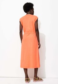 Robe orange, longueur genou, avec des manches courtes et une taille élastique. Texture douce. Portée avec des sandales multicolores. Design simple et décontracté.
