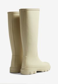 Bottes hautes en caoutchouc beige avec une finition texturée, un bout arrondi, une semelle rainurée et des lignes verticales discrètes sur la tige. Logo "HUNTER" sur le talon.