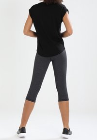 Černý top s krátkými rukávy spárovaný se šedými tříčtvrtečními legínami a černými teniskami. Legíny mají hladkou texturu a přiléhavý střih.