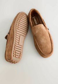 Chaussures à enfiler en suède marron avec des semelles en caoutchouc texturé, bout arrondi et couture décorative le long des bords. Design plat et décontracté.