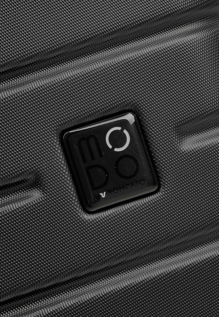 Acercamiento a una maleta negra texturizada con un logo negro cuadrado que dice "MODO by Roncato" en su superficie.