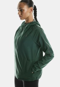 Roheline kerge jakk kapuutsiga, mis sisaldab vetsiluku, küljetaskuid ja peegeldavaid aktsente varrukatel. Sile tekstuur.