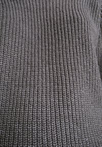 Gros plan sur un tissu gris tricoté avec une texture côtelée verticale et un motif de points étroitement tissés.
