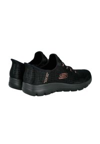 Zapatillas negras sin cordones hechas de material texturizado, con un patrón de cocodrilo y una suela acolchada. Con detalles en color oro rosa.