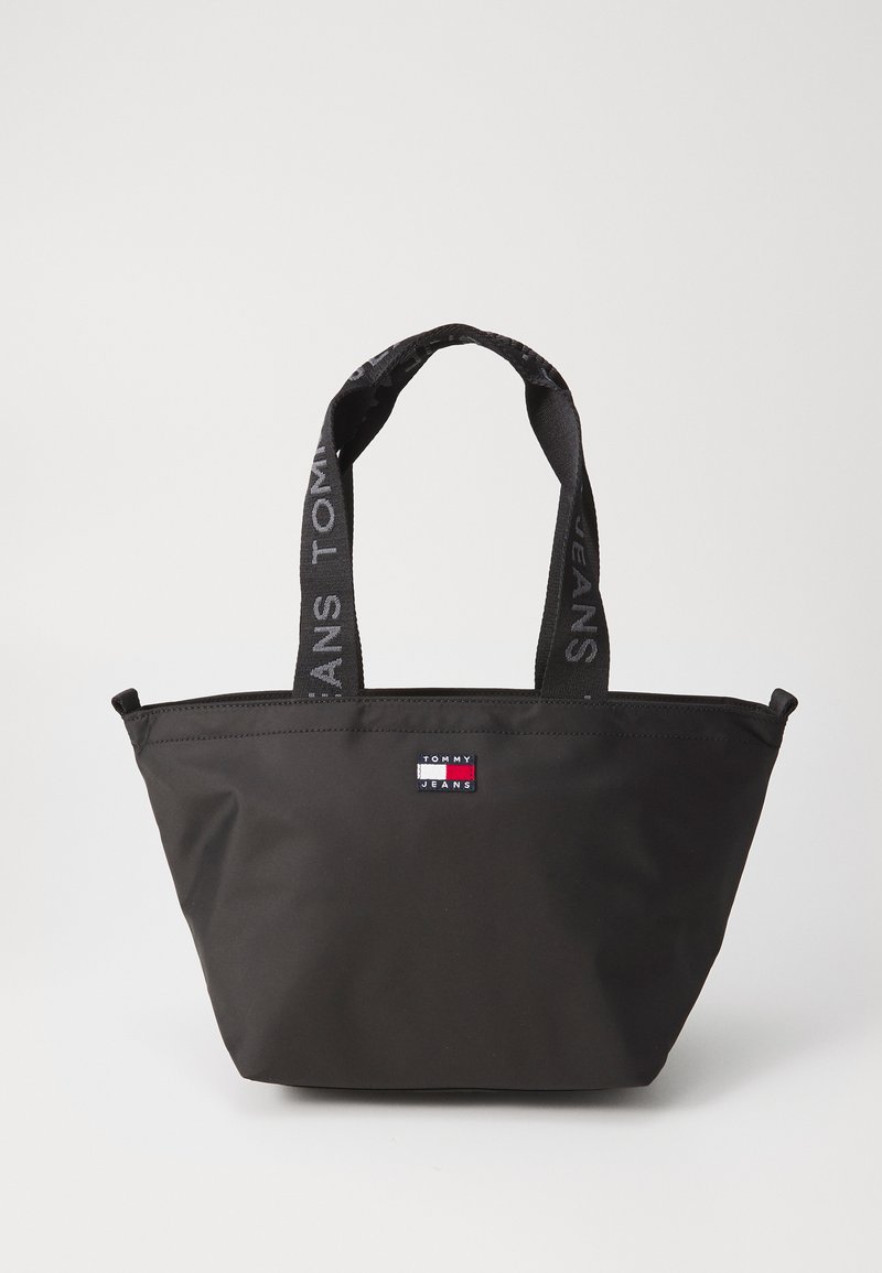 Schwarze Tragetasche aus strapazierfähigem Stoff, mit zwei schwarzen Griffen und dem Aufdruck "TOMMY JEANS". Sie hat eine rechteckige Form und ein Marken-Logo-Patch.