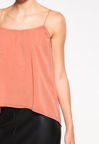Top senza maniche color pesco con spalline sottili, tessuto leggero e vestibilità ampia. L'orlo è leggermente più lungo sul retro.