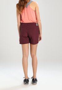 Maroone shorts med en tætsiddende design og to bagsider lommer, parret med en lyserød tanktop med en lys grå strop. Sorte træningssko.