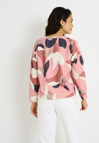 Sudadera rosa con un patrón floral abstracto en azul marino, blanco y burdeos. Presenta un tejido texturizado y mangas largas, con un dobladillo que se sitúa a la altura de la cintura.