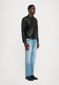 Melnas ādas jaka ar apkakles dizainu, kas aprīkota ar divām priekšējām kabatām un pogām. Valkāta kopā ar gaiši zilām taisnām biksēm un melniem apaviem.