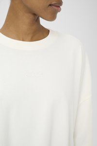 Crème-kleurige sweatshirt van zachte stof met een ronde hals en een oversized pasvorm. Beschikt over een klein, geborduurd logo op de voorkant.