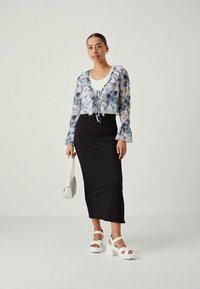 Ljusblå och vit blommig genomskinlig blus med volangkrage, kombinerad med en svart figurnära kjol och vita blockklackade sandaler.