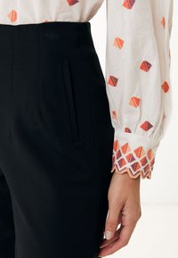 Svarta tapered byxor med sidofickor, i kombination med en vit skjorta som har flerfärgad diamantbroderi och scallopade manschetter.