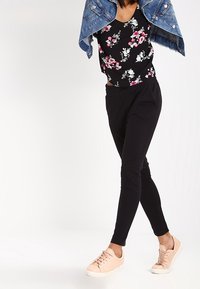 Haut noir à fleurs avec un col en V, pantalon de jogging noir et baskets rose clair. Veste en denim drapée sur les épaules, look chic et décontracté.