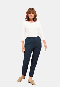 Marineblauwe op maat gemaakte broeken met zakken, gecombineerd met een witte lange mouwen top. Beige loafers met een kettingaccent maken de outfit compleet.