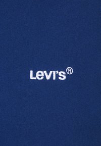 Tela azul con una textura suave que presenta el logotipo bordado en blanco "Levi's®". Diseño sencillo, sin patrones ni acentos adicionales.