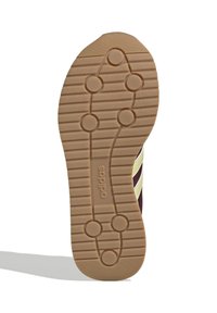 Sula av vinröda sneakers med beige detaljer, som har en texturerad gummiyta med cirkulära och linjära mönster för bättre grepp.