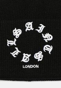 Gorra de punto negra con texto bordado en blanco en un patrón circular. Entre sus características se incluyen diferentes estilos de letras y la palabra "LONDRES" en la parte inferior.