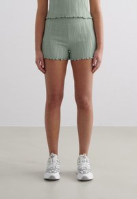Shorts en vert clair texturé avec un ourlet festonné, associés à un haut assorti. Des chaussures de sport blanches complètent la tenue.