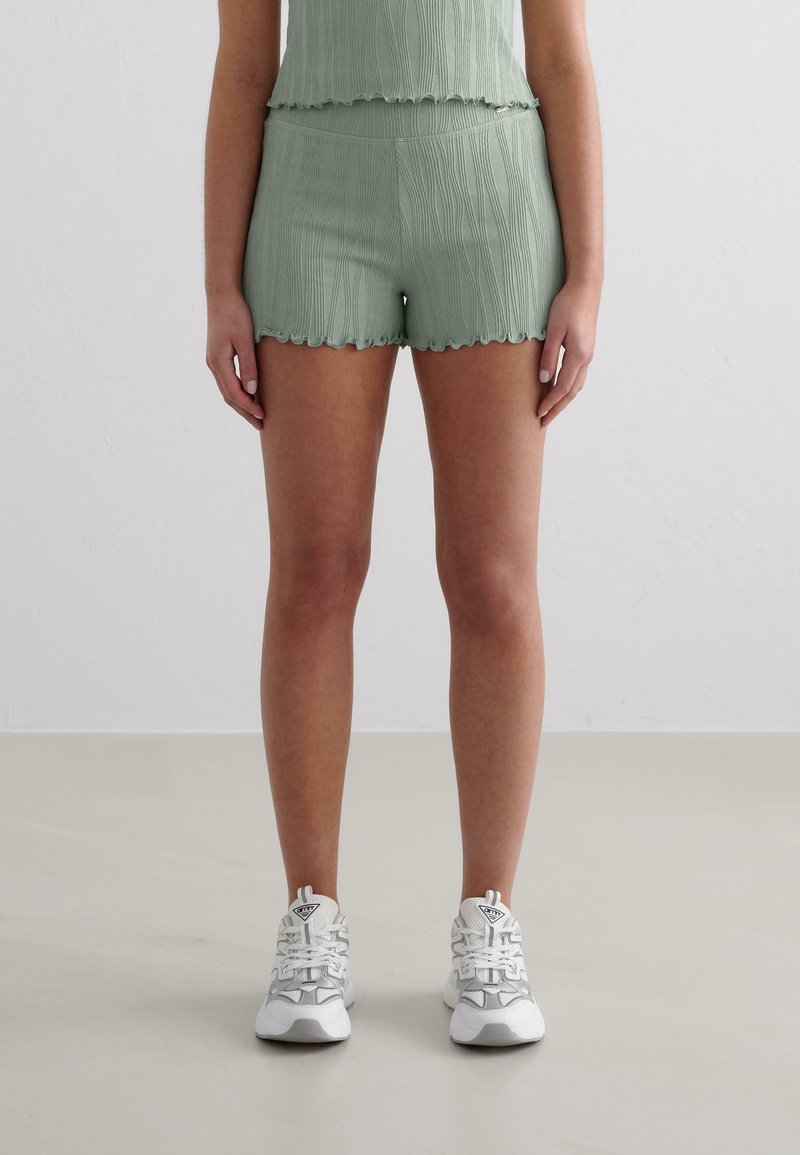Shorts en vert clair texturé avec un ourlet festonné, associés à un haut assorti. Des chaussures de sport blanches complètent la tenue.