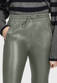 Lichtgroene nep leren broek met een elastische tailleband en een trekkoord, voorzien van zijzakken en een soepele, glanzende textuur.