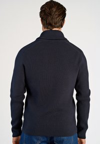 Marineblauer gerippter Pullover mit hohem Kragen. Das strukturierte Material ist warm und dehnt sich leicht, mit langen Ärmeln und einem geraden Saum.