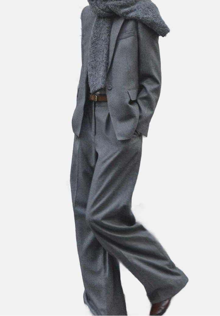 Personne portant un costume gris avec un pantalon à jambes larges, un blazer assorti, une ceinture marron, des chaussures marron et une épaisse écharpe grise enroulée autour du cou.