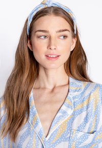 Lyseblå pyjamasoverdel med abstrakte mønstre i gul og hvid, med en notch krave og en frontlomme. Matchende mønstret hårbånd.