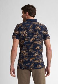 Marinblå polo med gyllene blommor och bladmönster, korta ärmar och krage. Tyget verkar mjukt med en figurnära design.