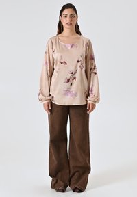Blusa beige a maniche lunghe con motivi floreali, abbinata a pantaloni larghi marroni. Tessuto morbido, vestibilità rilassata e design con scollatura rotonda.
