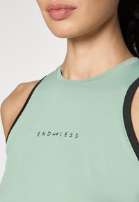 Mint green sleeveless top with black trim, featuring the text "ENDLESS" in black on the front. Smooth, stretchable material.