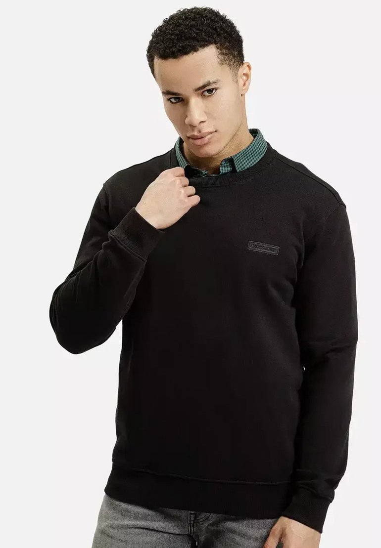 Czarna bluza z teksturowanej tkaniny, z okrągłym dekoltem i małym logo na piersi, uzupełniona zieloną koszulą w kratę noszoną pod spodem.