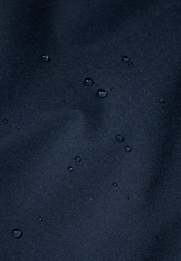 Tissu navy résistant à l'eau avec une texture lisse, présentant plusieurs petites gouttes d'eau à la surface, indiquant des propriétés hydrophobes.