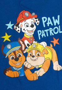 Maglietta blu a maniche corte con cani cartoon in abbigliamento da soccorso: un dalmata, un cane marrone e un bulldog con accenti colorati e stelle.