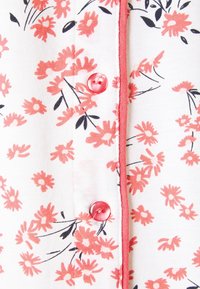 Floral patterned fabric with pink and black flowers on a white background. Features a pink button and contrasting trim along the button placket.