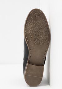 Černá podrážka boty s texturovaným vzorem zahrnujícím květinové motivy, kulatým tvarem a kontrastní hnědou gumovou podrážkou. Uvedena velikost 37.