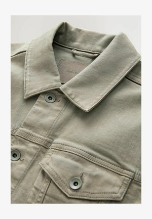 Khaki-Jeansjacke mit spitzem Kragen, zwei Brusttaschen und Knopfverschlüssen. Der Stoff hat eine weiche Textur und matte Oberfläche.