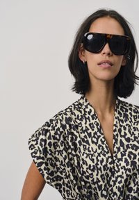 Leopardenprint blouse met korte pofmouwen in crème en zwart. Model draagt oversized schildpaddenbril. Soepele stof textuur.