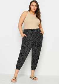 Svarta mönstrade byxor med elastisk midja och fickor, med en geometrisk design i vitt, kombinerat med en beige linne.