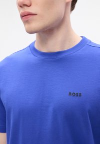 Μπλε βαμβακερή μπλούζα με στρογγυλή λαιμόκοψη και κοντά μανίκια. Διαθέτει το μαύρο λογότυπο "BOSS" στην αριστερή περιοχή του στήθους. Ίσια υφή.