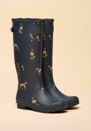 Marinblå vattentäta gummistövlar med ett mönster av olika hundar. Texturerad yta med en robust svart sula och en märkt flik på sidan.
