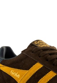Sneaker in suede marrone con accenti gialli e collare imbottito, caratterizzato da un logo sulla linguetta e superfici testurizzate. Design classico con lacci.