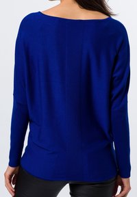 Pull en tricot bleu avec un large col, des épaules tombantes et une rayure verticale texturée dans le dos. Poignets et ourlet ajustés.