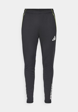 Sorte atletiske bukser med slim fit, der har et hvidt logo, grønne detaljer og hvide striber ned langs nederste del af benene. Blød stoftekstur.