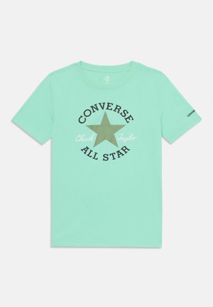 Piparmētru zaļš T-krekls, kas izgatavots no kokvilnas, ar apaļu kakla izgriezumu, kuram ir liels apdrukāts zvaigzne un "Converse All Star" teksts melnā un baltā krāsā.
