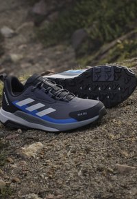 Ζεύγος μαύρα και μπλε παπούτσια adidas Terrex για τρέξιμο σε μονοπάτια πάνω σε πετρώδες έδαφος, με αντιολισθητικές σόλες και σχέδιο με κορδόνια.