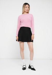Rosa, fluffy genser med lange ermer, kombinert med et svart, utsvingt mini-skjørt. Modellen har på seg hvite sokker og svarte hælsko.