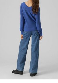 Maglione azzurro lavorato a maglia con scollo a V e maniche lunghe, abbinato a jeans in denim a gamba larga. La modella indossa scarpe platform nere.