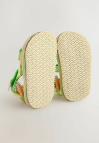 Grüne weiche Sandalen mit strukturierten Gummisohlen und verstellbaren Verschlüssen. Die Sohlen haben ein wellenförmiges Muster für besseren Halt.